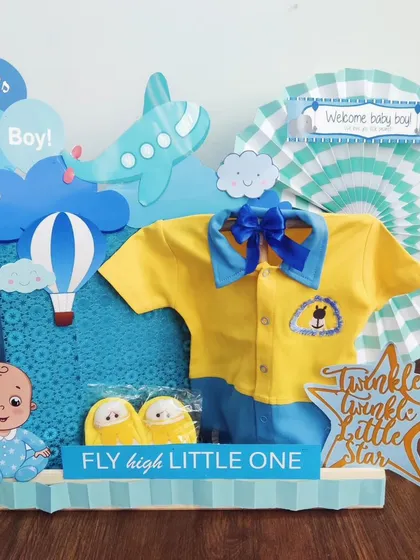 'Fly High Little One!' This aviation-themed hamper is perfect for a little adventurer. It includes a cute yellow and blue outfit, matching slippers, and airplane decorations.