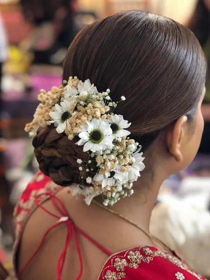 A clear, detailed shot of a braided floral bun. This hairstyle combines the structure of a braid with the softness of fresh flowers, perfect for a romantic bridal look.
