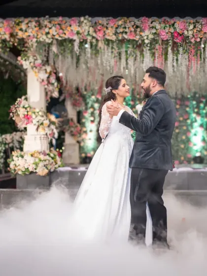 A magical first dance, surrounded by smoke and beautiful floral decorations. This wide shot captures the fairytale atmosphere of the wedding reception.