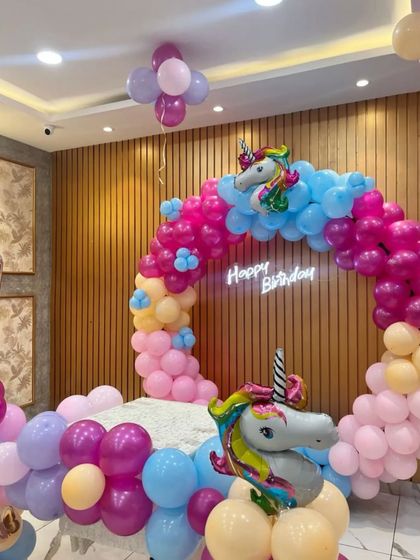A vibrant unicorn-themed balloon ring. This decoration uses bright pink, blue, and purple balloons, with two large unicorn foil balloons and a subtle neon "Happy Birthday" sign.