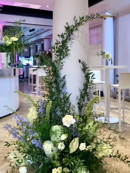 A free-flowing, natural-style arrangement for a modern event. This design uses tall greenery and a mix of white and light purple flowers to create an organic, garden-inspired look.