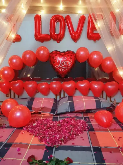 A close-up of the bed in a romantic setup, showing the 'LOVE' foil balloons, heart-shaped balloons, and a heart made of rose petals. It's all in the details when it comes to creating a memorable surprise.
