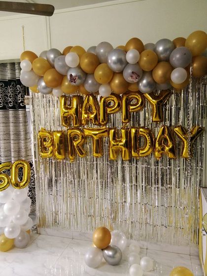 A simple yet classic 60th birthday decoration. This setup uses a silver foil curtain backdrop with gold 'Happy Birthday' foil letters and a gold and silver balloon garland.