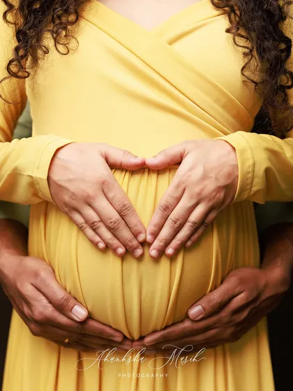 A symbol of love and anticipation. This close-up maternity portrait focuses on the hands of expecting parents forming a heart, a simple yet powerful expression of the life they are creating together.