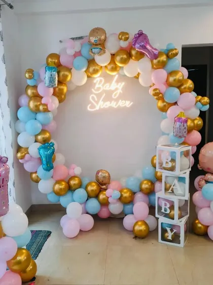 This vibrant baby shower decoration features a full circular balloon arch in pink, blue, white, and gold. The design is centered around a "Baby Shower" neon sign and includes transparent "BABY" blocks and character foil balloons, creating a complete and festive photo corner.