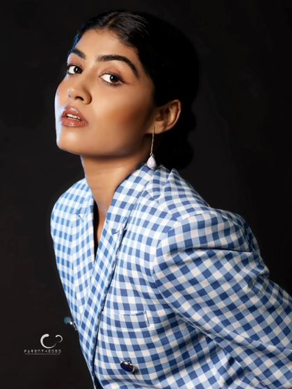 A classic beauty portrait with a strong, confident gaze. The simple black background makes the blue and white pattern of the suit stand out.