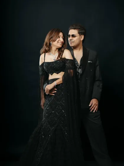 An elegant studio portrait capturing a quiet, loving gaze between the couple. The sophisticated black attire and the simple black background put the focus entirely on their connection, resulting in a classic and romantic photograph.
