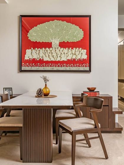 The dining area is centered around a beautiful wooden table and sleek chairs. The space is elevated by a custom-made 'Tree of Life' art piece from Rajasthan, adding cultural elegance and symbolism.