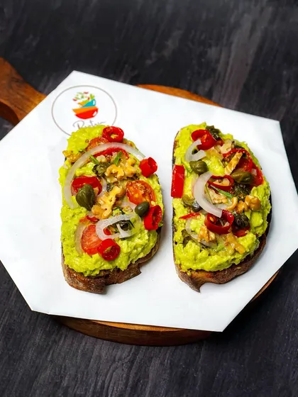 A close-up of the avocado toast, showcasing the colorful and fresh toppings. The dark, rustic background makes the dish feel artisanal and wholesome.