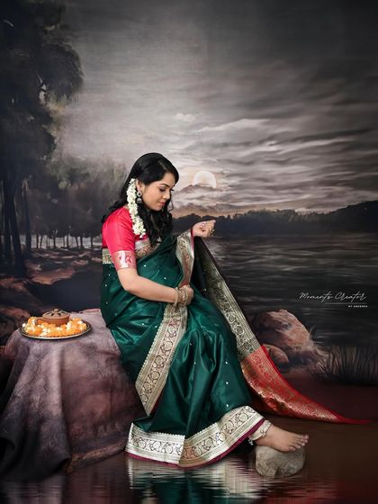 A quiet moment of reflection. Seated against a painted landscape, the mom-to-be in her saree looks down, creating a serene and contemplative portrait.