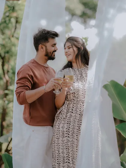 A celebratory toast to their future together. This shot captures a simple, happy moment during a relaxed outdoor pre-wedding session, framed by soft white drapes.