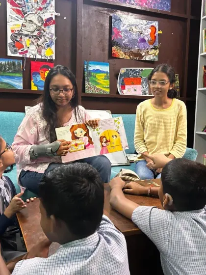 A group of children gathers around a table with a volunteer, pointing at the pictures in a book. These small, focused group interactions allow for personal connection and deeper engagement with the story.