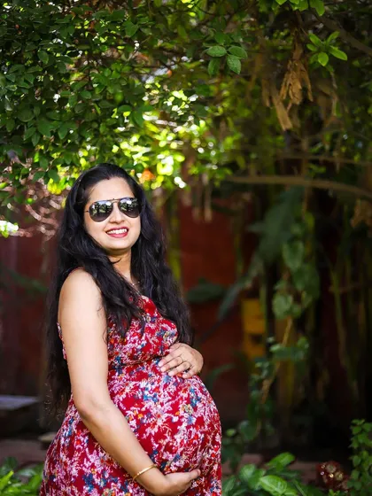 A confident and happy solo maternity portrait. The combination of the vibrant red floral dress, sunglasses, and the natural setting gives this photo a relaxed and stylish feel, perfect for capturing the personality of the mother-to-be.