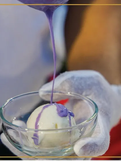 Scooping up smiles, one scoop at a time. A chef pours a vibrant purple sauce over a scoop of ice cream, creating a visually appealing and tasty treat.