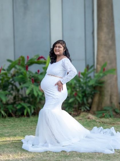 A beautiful, smiling portrait of a mom-to-be in a white mermaid-style gown in a green park.