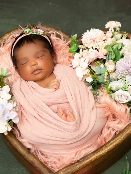 This classic newborn portrait captures a baby sleeping peacefully in a heart-shaped wooden bowl, surrounded by a bed of soft pink fur and delicate flowers. This style emphasizes your baby's serene and angelic features.