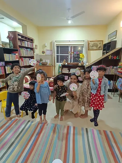 A wider view of the children showing off their beautiful dot paintings, with our book-filled shelves creating an inspiring backdrop.