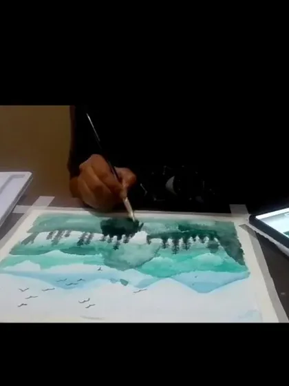 A student participating in one of our online watercolor classes, learning to paint a forest and lake scene from home.