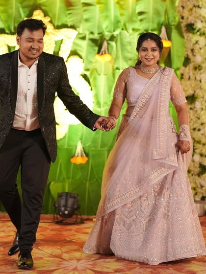 A happy couple walking hand-in-hand at their reception. The bride is wearing a beautiful light pink lehenga, perfectly complementing the groom's sparkling blazer.
