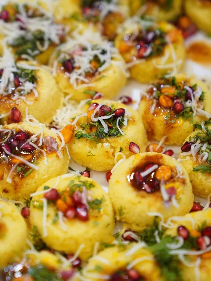 A close up of our beautifully garnished dhokla chaat. These bite sized pieces are topped with chutneys, sev, and pomegranate seeds, creating a perfect appetizer.