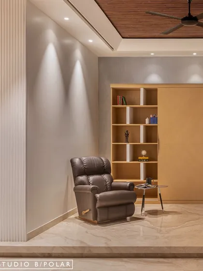 On the opposite side of the lounge, a comfortable leather recliner offers a perfect spot for relaxation. The TV wall features sliding panels that can conceal the screen, transforming it into a display unit.