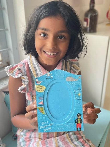 A happy girl holds up the pirate-themed photo frame she created using decoupage techniques. A fun way to frame your favorite memories.