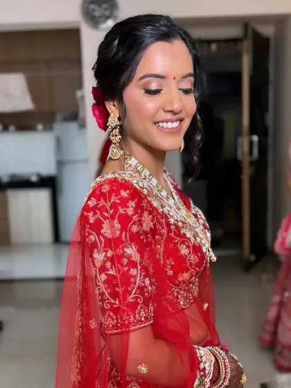 A smiling bride with her hair in a soft, side-parted updo, complemented by a red rose. This style is perfect for framing the face and highlighting a joyful expression.