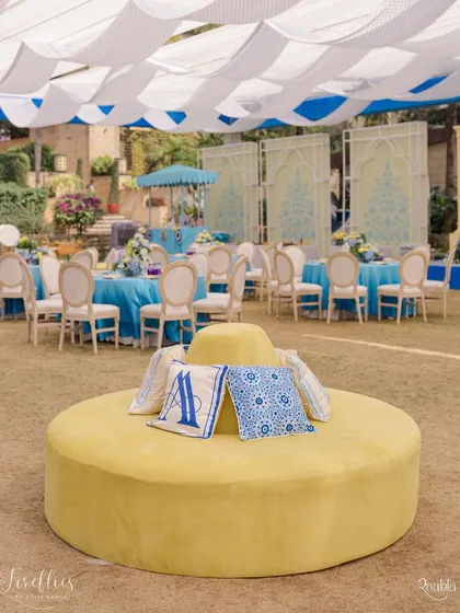A central yellow ottoman with custom monogrammed cushions in the signature blue and white of the Jodhpur-themed Haldi. This piece served as a stylish and comfortable focal point in the lounge area.