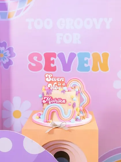 A close-up of the "Too Groovy for Seven" birthday cake, perfectly matching the retro-pastel theme with its rainbow and flower decorations.