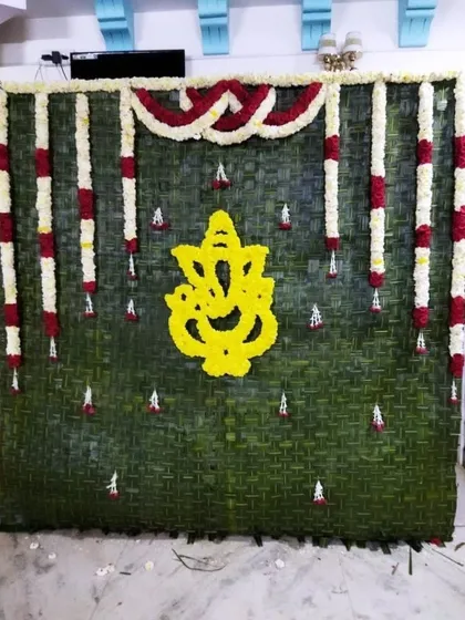 I create unique, natural backdrops for poojas and home events, such as this wall made of fresh banana leaves featuring a Ganesha motif crafted from yellow flowers.