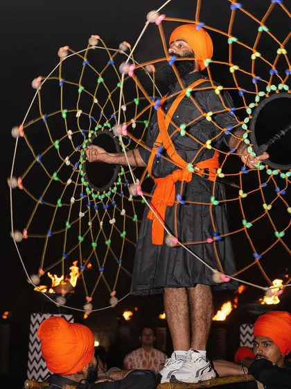A captivating performance during the Jaago night. A Sikh performer showcases a traditional art form with a large, illuminated prop, adding a spectacular visual element to the birthday festivities.