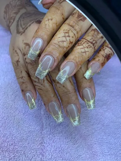 A close-up of the elegant gold glitter French tips against a henna-adorned hand.