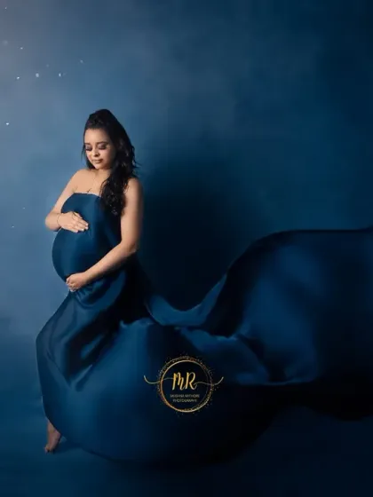 An artistic shot against a deep blue, starry backdrop. The mother-to-be cradles her bump, wrapped in a swath of matching blue fabric that pools around her.