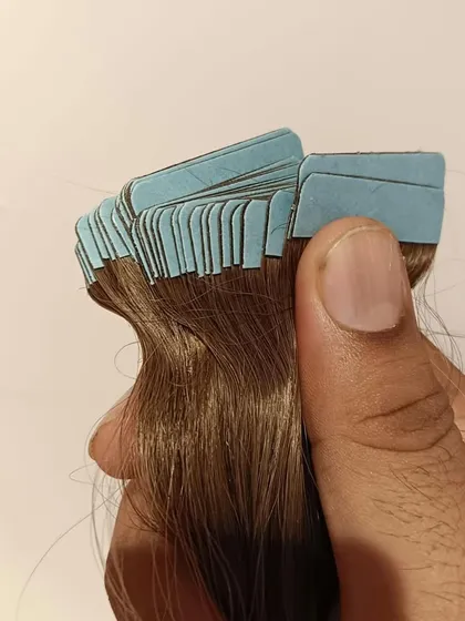 Holding a set of tape-in extensions, this image highlights the neatly aligned tabs. This precision ensures a smooth and seamless application process for hair stylists.