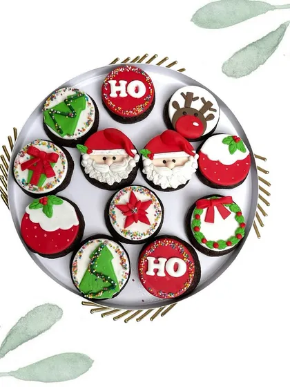 A dozen festive cupcakes to sweeten your holiday season. Each one is decorated with a unique Christmas design, from Santa and his reindeer to wreaths and trees.