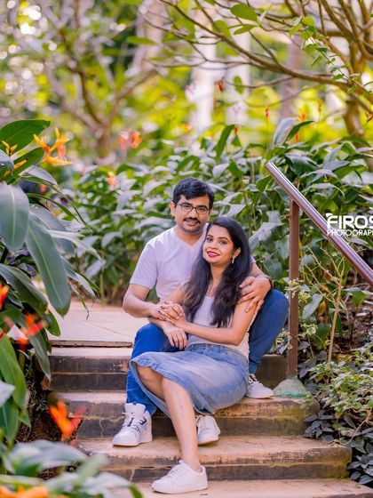 A relaxed and casual couple's portrait on a stone staircase surrounded by lush greenery and orange flowers.