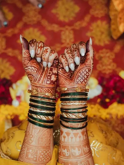 A detailed shot of the bride's hands, showcasing the intricate mehendi design and traditional green bangles.