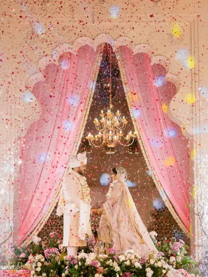 A shower of confetti rains down on the couple during their varmala ceremony under a grand archway at Alila Bishangarh, a moment of pure magic and celebration.