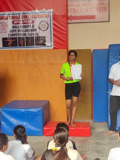 Twarita Shah stands on the podium to receive her certificate at the MSSA Mallakhamb Competition. This moment on the victory stand is a powerful reward for her consistent hard work and training.
