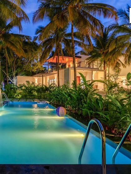 A view of the villa's pool at dusk, surrounded by palm trees and tropical plants. I design the entire property, including outdoor spaces, to ensure a cohesive and luxurious experience.
