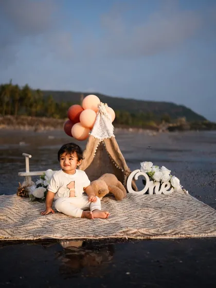 A happy, seated portrait of the baby boy celebrating his first birthday. The combination of the 'One' sign, balloons, and his sweet smile makes for a perfect milestone photograph.