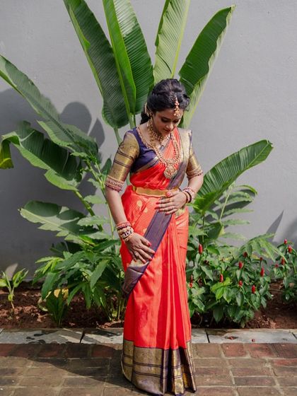 A full-length view of the bride in her orange and navy blue Kanchipuram saree. The traditional color combination is both bold and beautiful.