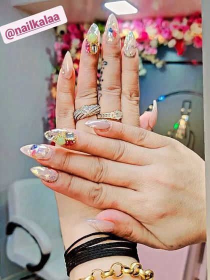 A highly detailed and artistic set of stiletto nails. The design features a nude base with encapsulated glitter, colorful abstract art, and 3D embellishments.
