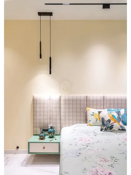 A close-up detail of the bedside area, showing the mix of textures and patterns. The fabric headboard, floral cushions, and sleek pendant lighting work together to create a corner that feels both cozy and stylish.