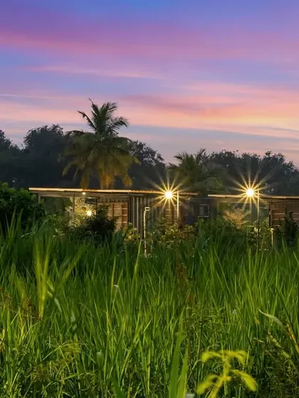 A container home at Suzo Farms in Chennai, set against a dramatic sunset over a lush green field. This shot captures the beauty and tranquility of living in a modern, sustainable home in a rural setting.
