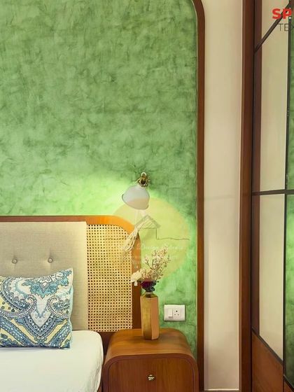 A detailed shot of the arched feature wall with green texture paint. The tufted cane headboard and simple wall sconce create a perfect blend of modern and traditional design elements.