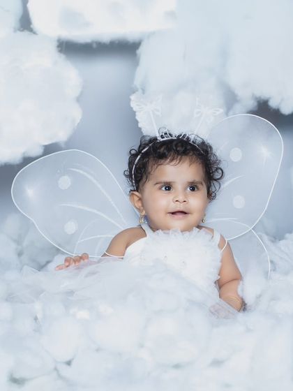 A sweet baby girl with angel wings, sitting among the clouds.