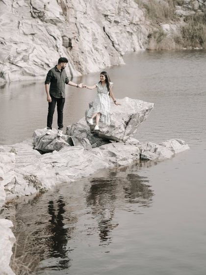 A beautiful wide shot of a couple holding hands across rocks in a quarry lake, their reflection visible in the water.