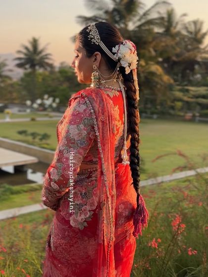 A stunning bridal look in a red floral saree, with a long, thick braid decorated with a mix of fresh flowers and traditional hair accessories.