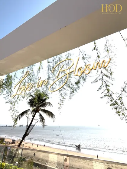 A still shot of the "Love in Bloom" sign against the bright sky and sea, a simple yet beautiful piece of decor for an outdoor wedding.